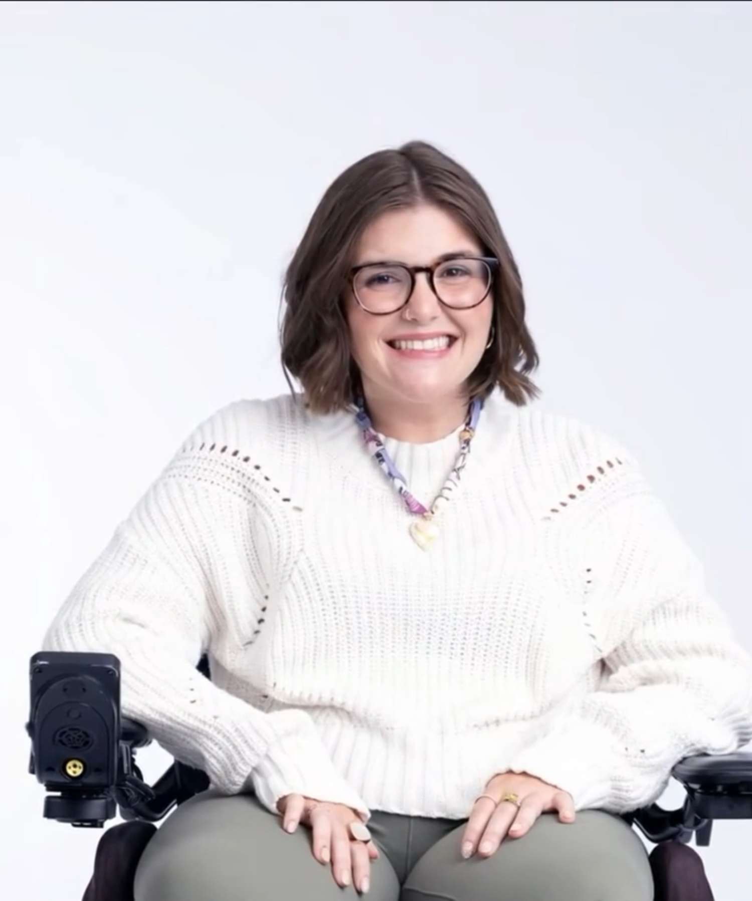An open book. On the left spread, Megan, a young woman with FA smiles while sitting in her wheelchair.